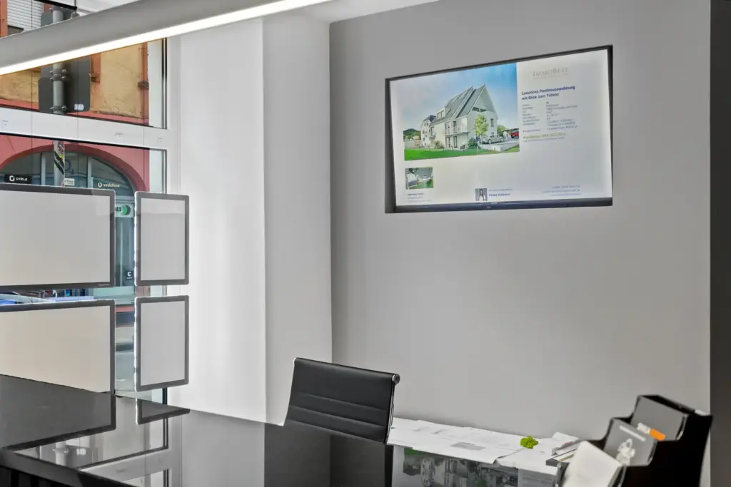 Immobilienangebote im Maklerbüro auf Bildschirmpräsentation.